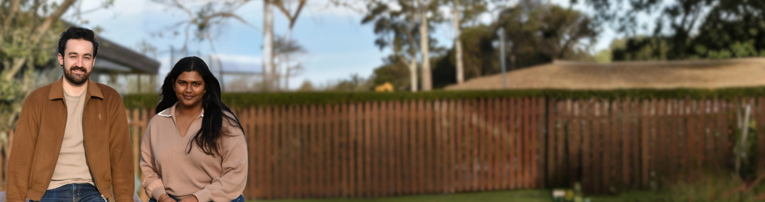 Promotional image banner for I-LEAD. Two people sitting on a park bench, facing the viewer. Behind them is a building, fence and landscape of trees and mountain