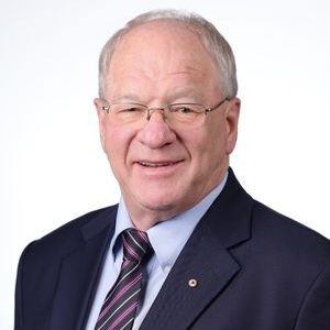 Image of a man with grey hair and glasses wearing a blue suit and tie, smiling at the camera.