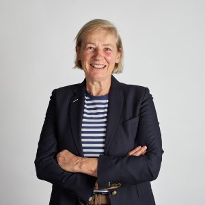 Portrait photo of Josie Chester, graduate of the I-LEAD Women in Industry 2025 program. Josie has blonde bobbed hair worn parted to one side, pale skin with rosy cheeks and blue eyes. She is standing with her arms gently folded, wearing a navy blazer, blue and white striped top and beige trousers.