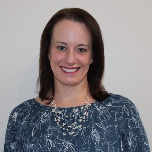 Portrait headshot of Belinda Venter, 2026 TLP Participant. Belinda has shoulder length straight brown hair, blue eyes and pale skin. She is looking directly at the camera and smiling showing teeth. She is wearing a round necked blue blouse with whilte floral outline print, and a pearl beaded fine wired multi-strand necklace