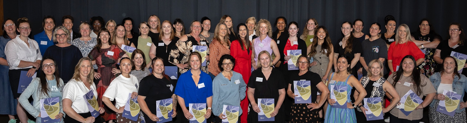 Group photograph of the I-LEAD Women in Industry 2025 graduates. The entire group of graduates are lined up in two standing and one kneeling row. Each woman is holding her certificate and has one hand on her hip/