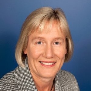 Formal portrait headshot of Sally Darke. Salle has a blonde bob with fringe, dark eyes and pale skin. She is smiling towards the camera.
