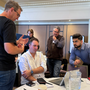 a group of people are standing and seated looking at a laptop and solving problems together
