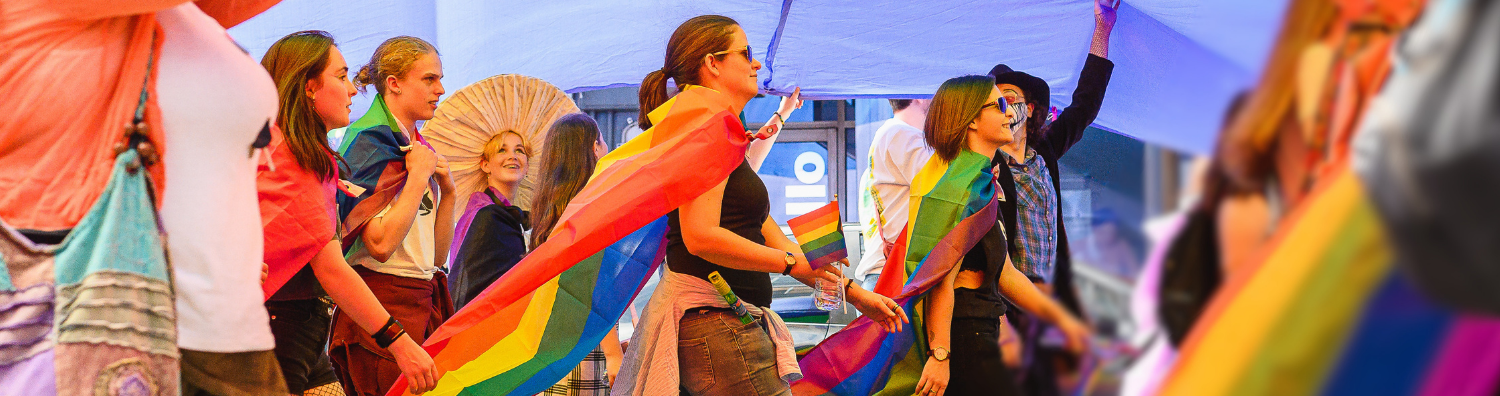 a group of people marching under a rainbow flag held high above their heads